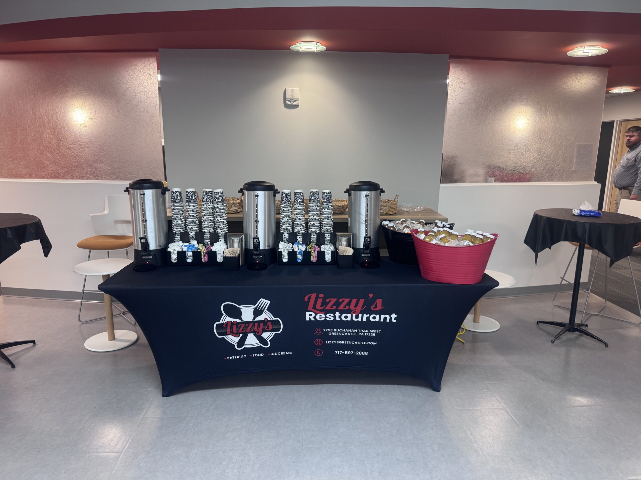 Lizzy’s coffee and juice station with coffee urns, stacked cups and bottled juices on a branded table